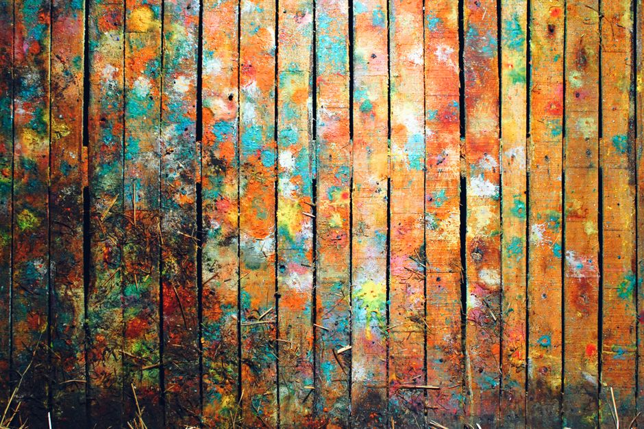 A vibrant and colorful rustic wooden panel with multi-hued paint splatters, perfect for artistic backgrounds.