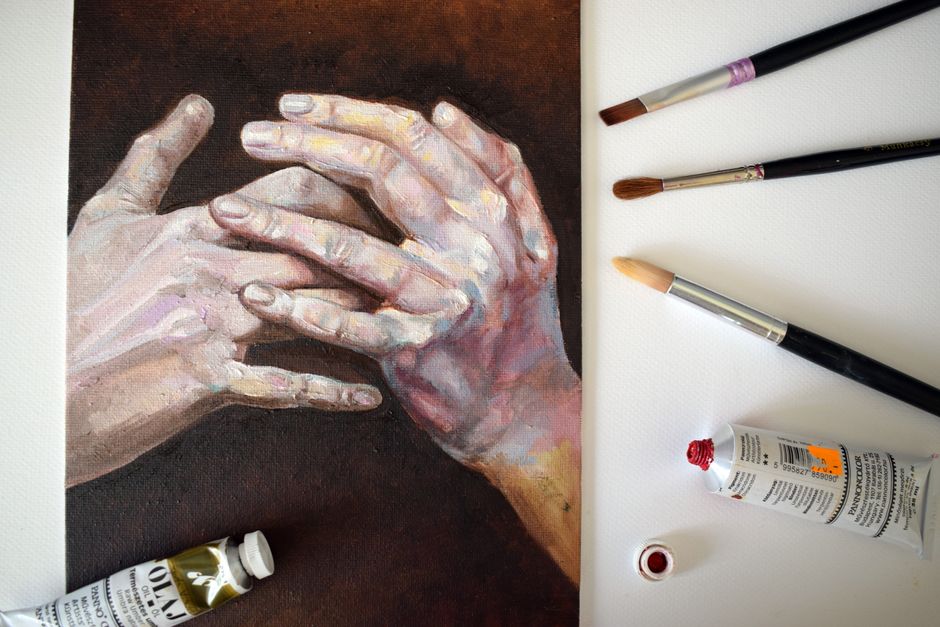 Close-up of a hand painting with brushes and oil paint tubes on a canvas.